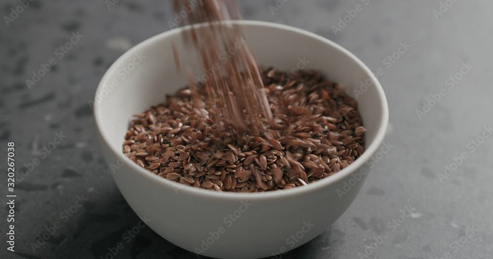 closeup flaxseed falling into white bowl on terrazzo countertop closeup flaxseed falling into white bowl on terrazzo countertop
