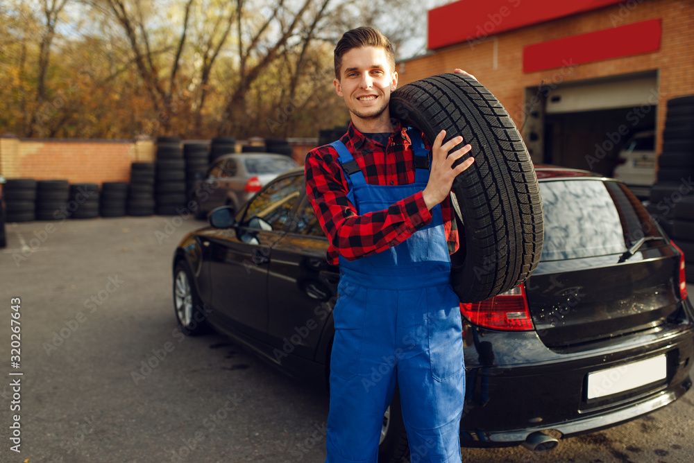 Male worker in uniform holds tyre, tire service Male worker in uniform holds tyre, tire service