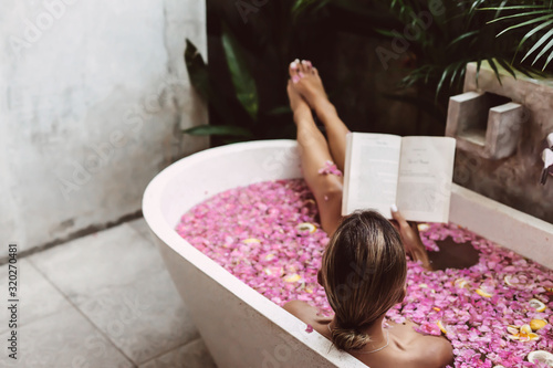 Fotografia Woman reading book while relaxing in bath tub with flower petals