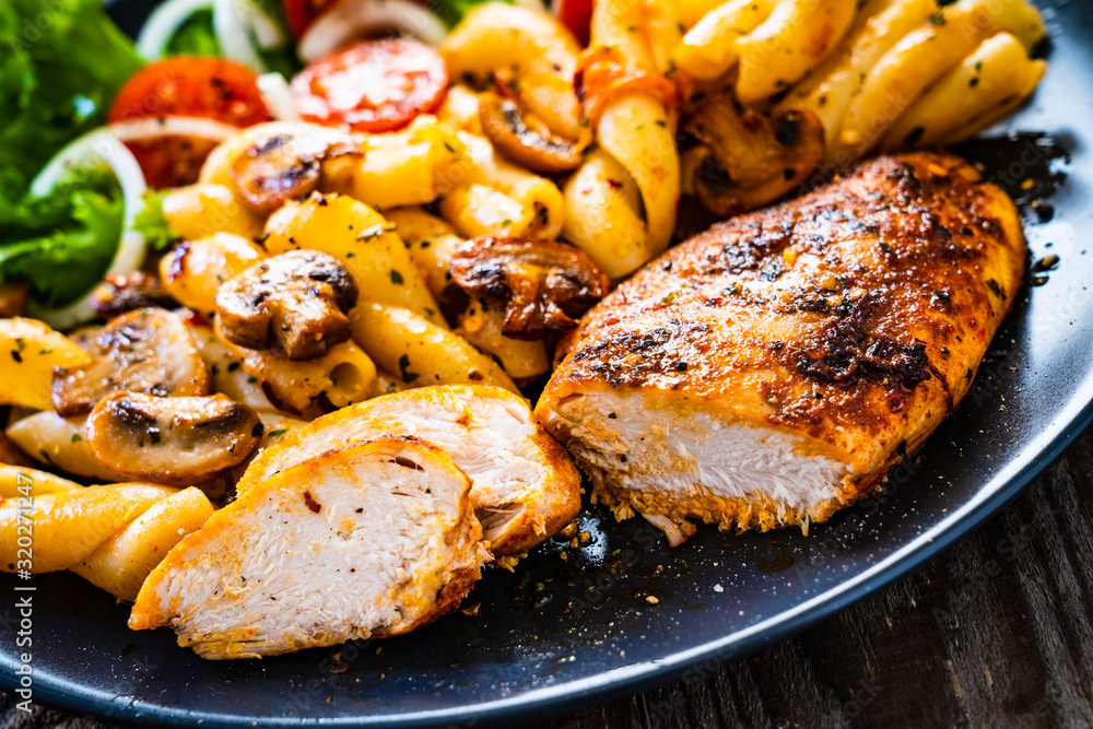 Roast chicken breast with pasta and vegetables on wooden background
