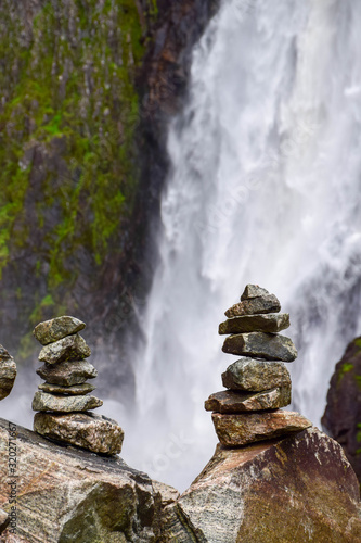 Stones meditation figures in front of the powerull Voringfossen waterfall. View from the bottom after a hike