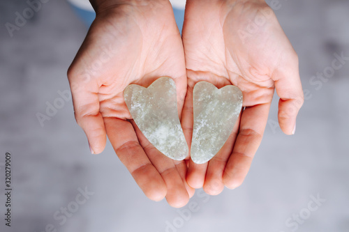 Foto Hands presenting gua sha stones over grey floor. Top view.