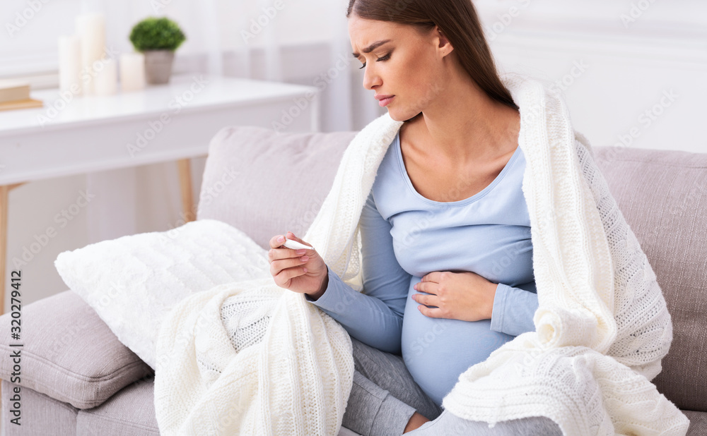 Unhappy Pregnant Lady Measuring Temperature Sitting On Couch At Home Unhappy Pregnant Lady Measuring Temperature Sitting On Couch At Home