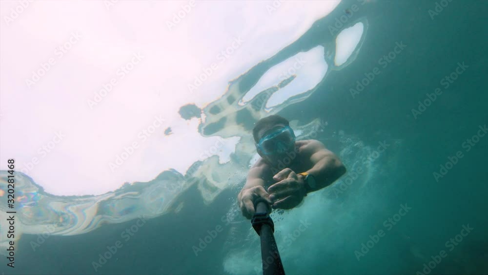 Muscular man in mask swims underwater, holding camera in front. Close-up. Muscular man in mask swims underwater, holding camera in front. Close-up.