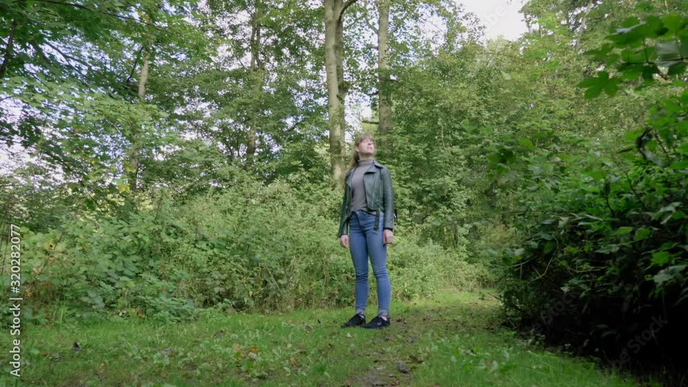 Young woman stands alone in green wood looking around, dolly Young woman stands alone in green wood looking around, dolly