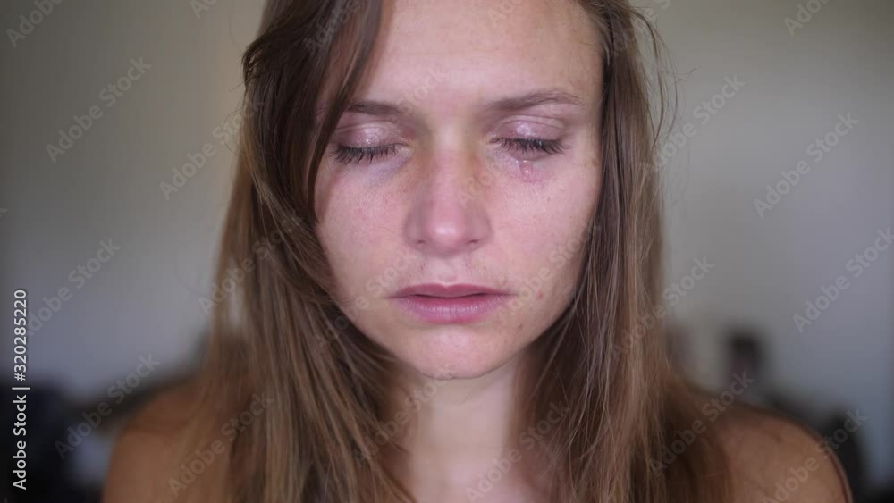 A close up, portrait shot of a young woman with wounds and bruises, looks and stares directly into the camera while a single tear is falling down from her eye onto her cheek and face. A close up, portrait shot of a young woman with wounds and bruises, looks and stares directly into the camera while a single tear is falling down from her eye onto her cheek and face.