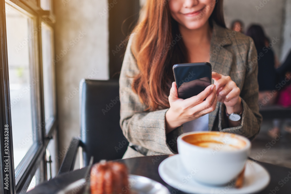 Closeup image of a woman holding and using mobile phone with coffee cup and snack on the table in cafe Closeup image of a woman holding and using mobile phone with coffee cup and snack on the table in cafe