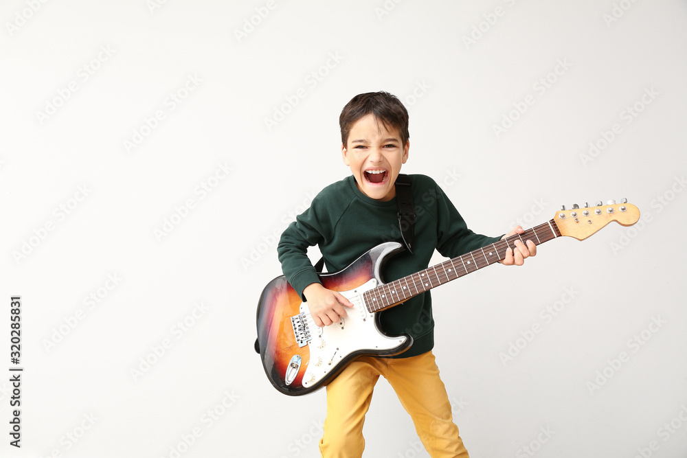 Emotional boy playing guitar on light background