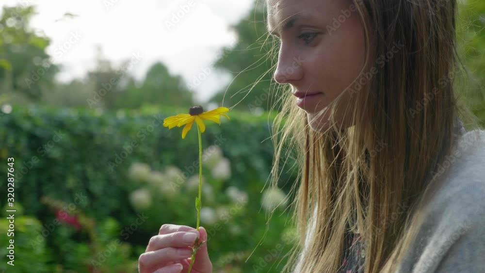 Beautiful young woman smiles at yellow daisy flower in hand, close-up Beautiful young woman smiles at yellow daisy flower in hand, close-up