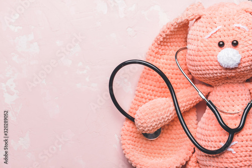 Stethoscope and baby toy on color background