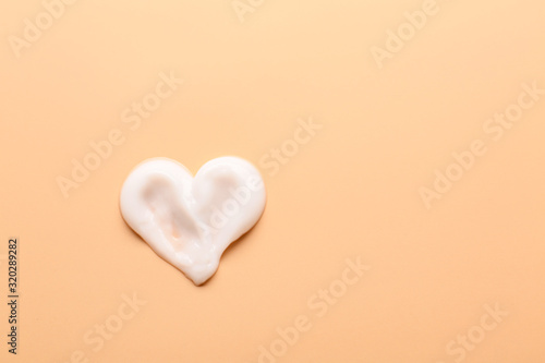 Heart made of cream on color background