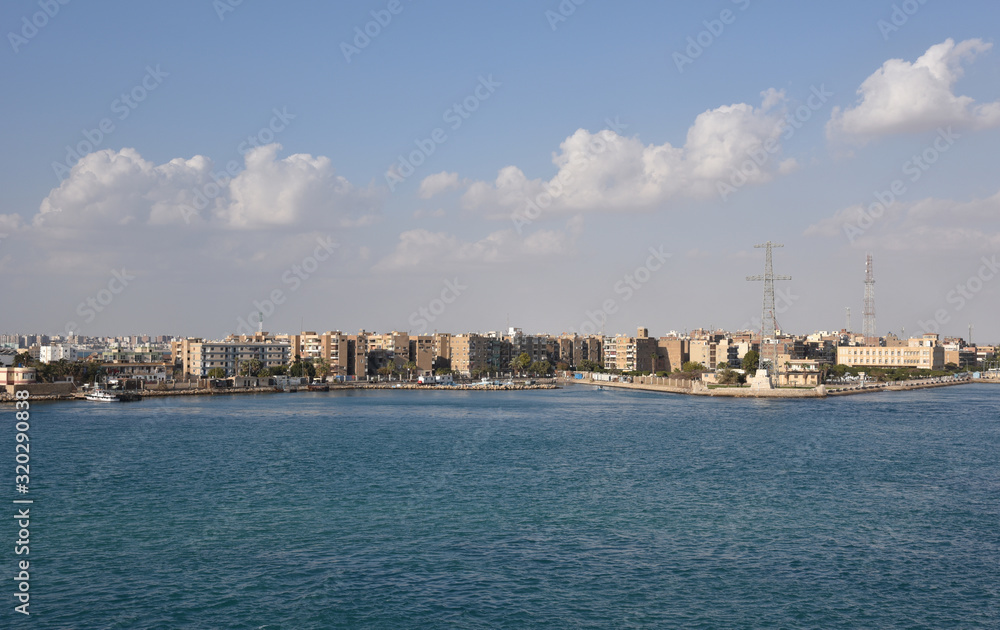 Suez Canal south entrance, view on the city  and transiting cargo ship. 