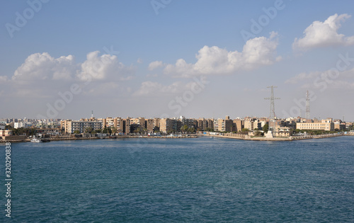 Suez Canal south entrance, view on the city and transiting cargo ship. 