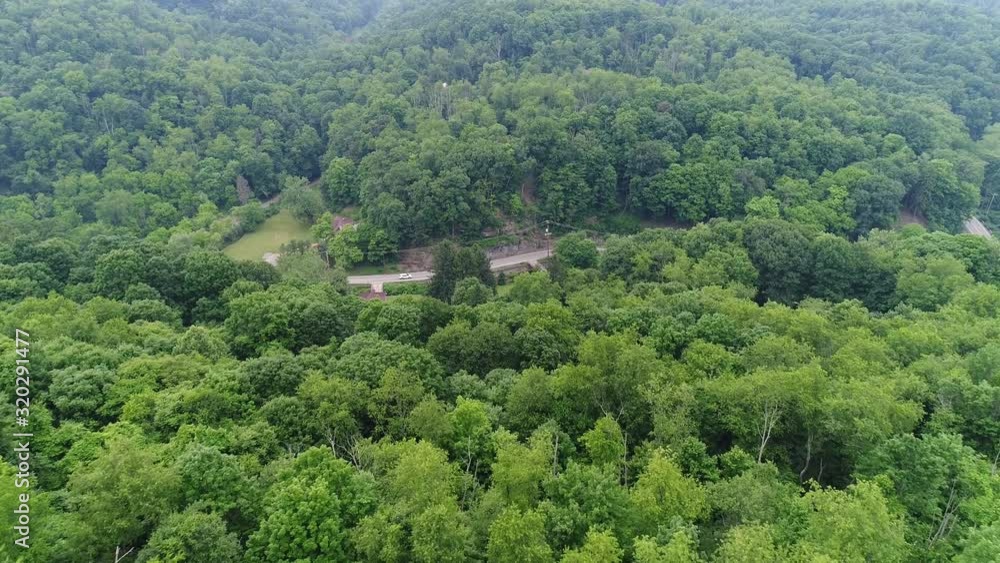 A slow forward aerial establishing shot of the Pennsylvania wooded countryside. Camera tilts down to reveal country road below. A slow forward aerial establishing shot of the Pennsylvania wooded countryside. Camera tilts down to reveal country road below.