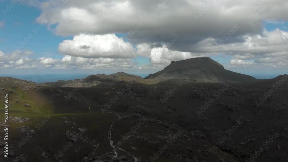 Aerial forward movement showing the rough terrain of the Itacolomi mountain tilting to focus on the trail below leading to the peak and mountain top ridge in Ouro Preto, Brazil Aerial forward movement showing the rough terrain of the Itacolomi mountain tilting to focus on the trail below leading to the peak and mountain top ridge in Ouro Preto, Brazil