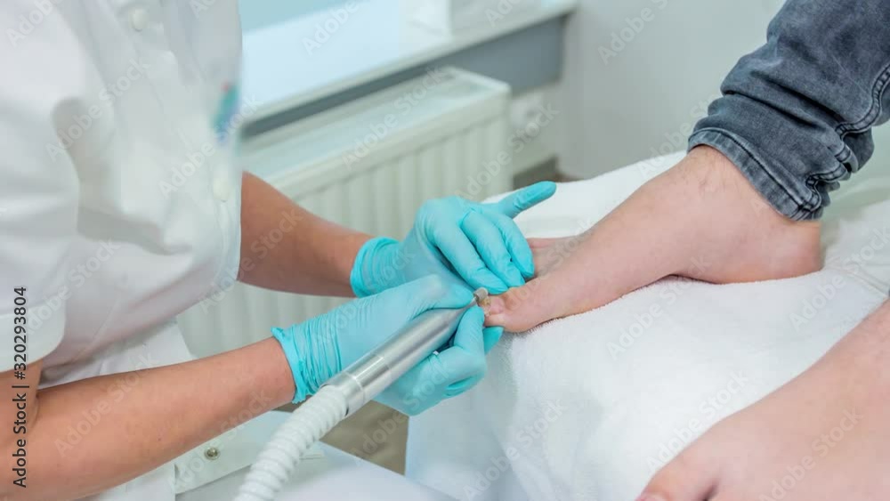 Pedicurist polishes nail plate on toenail with diamond nail drill electric machine Pedicurist polishes nail plate on toenail with diamond nail drill electric machine