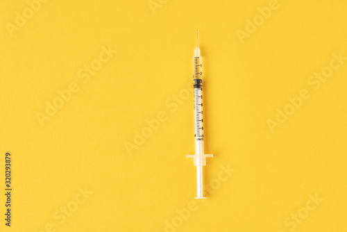 Medical syringe on the yellow background, top view with copy space. Vaccination and virus protection concept