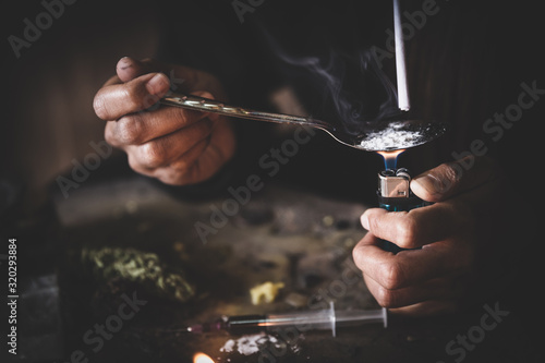 Drug addicts in the dark room. Addict/junkie preparing drugs with a spoon and lighter. White powder and a syringe. Drug concept. International drug abuse day.