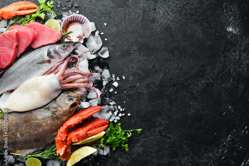 Fresh seafood and fish on black stone background. Flounder, lobster, squid, tuna, fish. Top view. Free copy space.