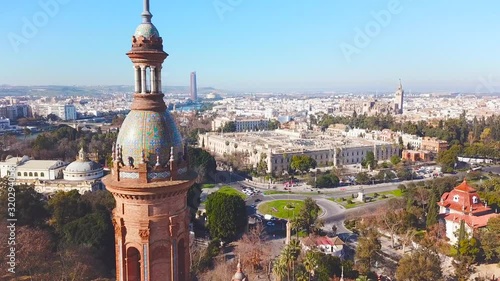 Generic cinematic aerial view of beautiful Spanish Square in centre of Seville. Close-up of tower. In background beautiful University of Seville, Cathedral of Seville and river Guadalquivir. Forward