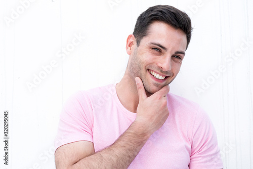 Close up handsome young man smiling by white background with hand on chin