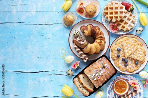Easter festive dessert table with various of cakes, waffles, sweets and strawberry. Blue background. Overhead view photo