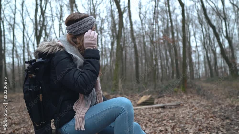 Young female caucasian photographer sitting on stump and touching her gray headband with her hand wearing pink glove Young female caucasian photographer sitting on stump and touching her gray headband with her hand wearing pink glove