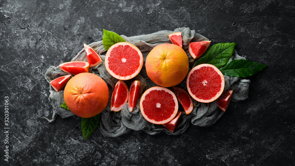Fresh juicy grapefruit with leaves. Citrus fruits on black stone background. Top view. Free copy space.