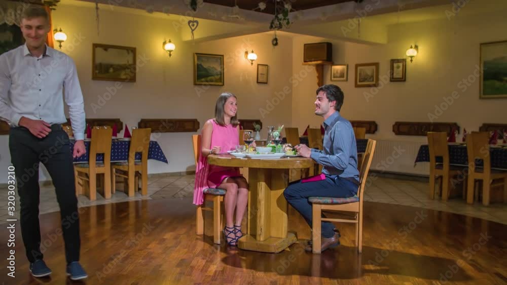 A waiter bringing the check to a restaurant table where a couple is having a dinner date A waiter bringing the check to a restaurant table where a couple is having a dinner date