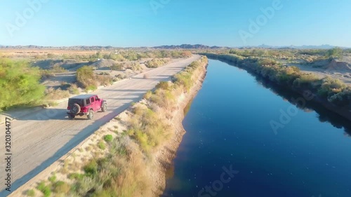 Close aerial view of  following a red SUV driving on road near Gila Gravity Irrigation Canal - Yuma, Arizona