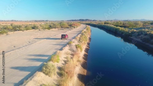 Low angle aerial view of  following a red SUV driving on road near Gila Gravity Irrigation Canal - Yuma, Arizona