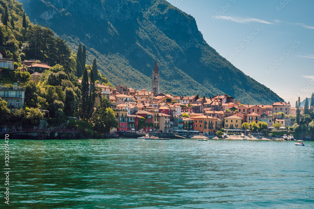 Beautiful panorama of the small town of Varena with its colorful houses and turquoise waters of Lake Como in the foreground, on a sunny summer day, Lombardy, Italy.
