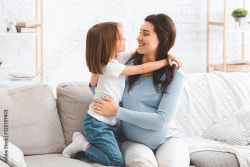 Little kid hugging pregnant mom, home interior © Prostock-studio