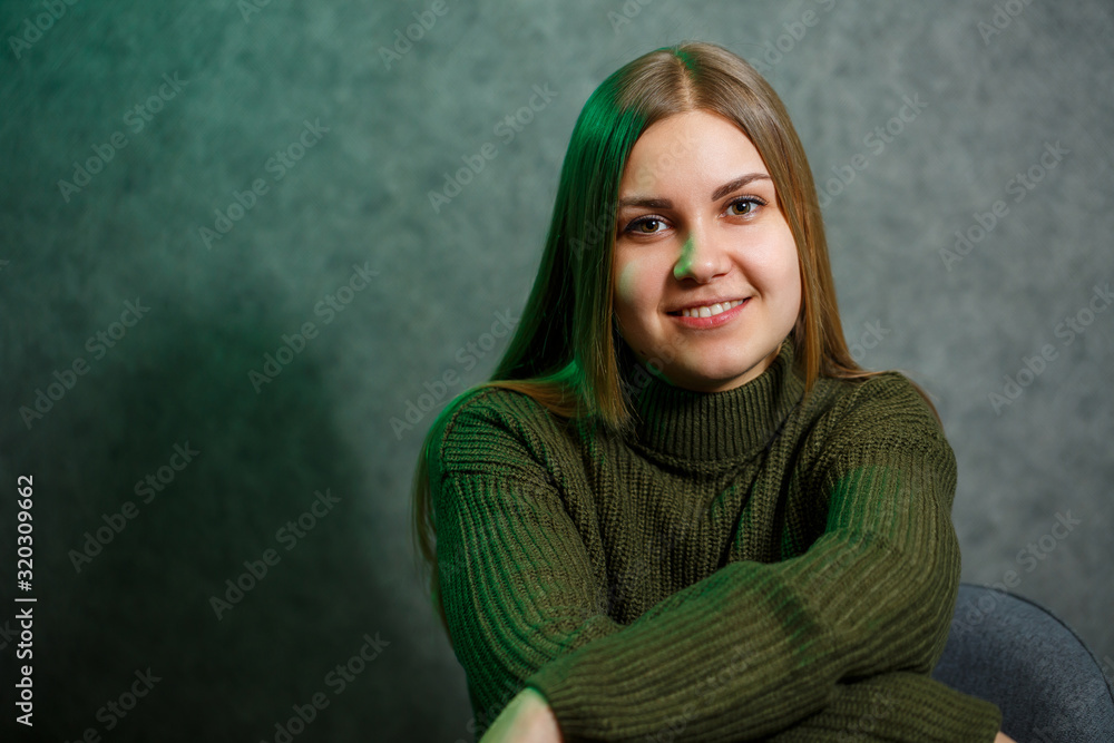Obraz premium Girl in a green sweater and jeans on a gray chair and smiling