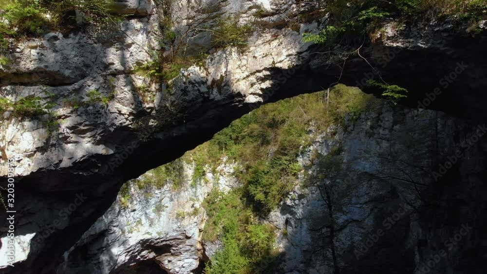 Aerial clip of the two people standing behind a railing on a cliff with semi vegetation. Natural bridge on Green Karst Aerial clip of the two people standing behind a railing on a cliff with semi vegetation. Natural bridge on Green Karst