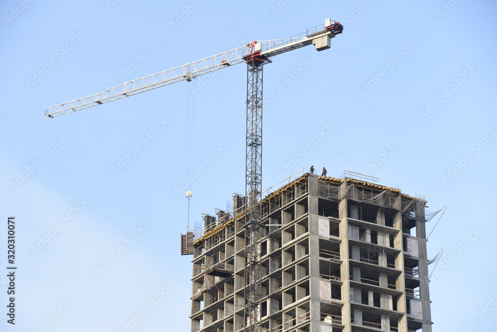 Tower cranes constructing a new residential building at a construction site against blue sky. Renovation program, development, concept of the buildings industry.