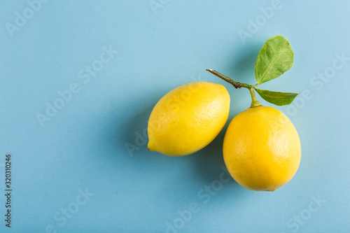 Two ripe lemons with a branch and leaves on a blue background. Top view.