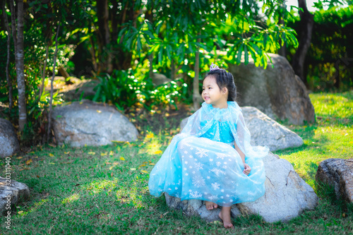 Portrait of cute smiling little girl in princess costume sitting on the rock in the park