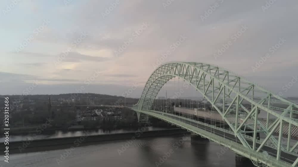 Runcorn Silver Jubilee Bridge aerial view at sunrise. Rising orbit left across waterfront scene. Runcorn Silver Jubilee Bridge aerial view at sunrise. Rising orbit left across waterfront scene.