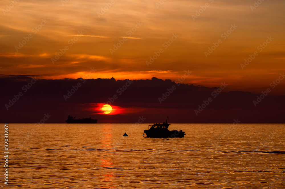 boat anchored over beautiful orange sunset background with cloudy skyline