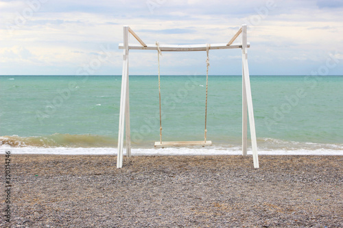 Empty wooden swing on the beach. Empty beach, blue sky.