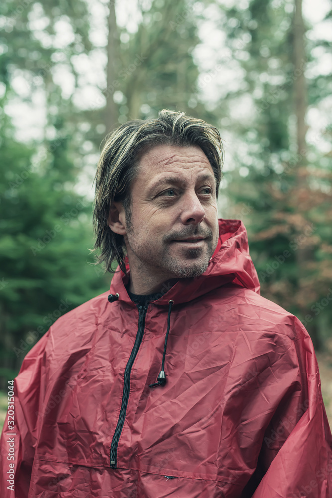 Smiling man in red raincoat in woods. Smiling man in red raincoat in woods.