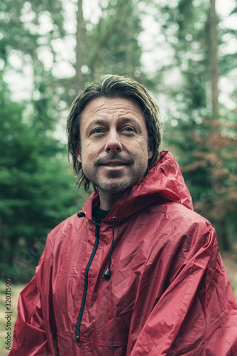Smiling man in red raincoat in woods.