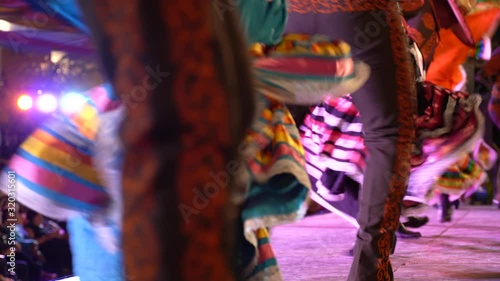 Camera pans left showing the beautiful chaos of Mexican dancers with flowing dresses.