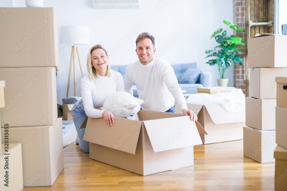 Young beautiful couple with dog sitting on the floor at new home around cardboard boxes Young beautiful couple with dog sitting on the floor at new home around cardboard boxes