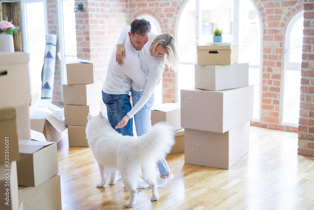 Young beautiful couple with dog hugging at new home around cardboard boxes Young beautiful couple with dog hugging at new home around cardboard boxes