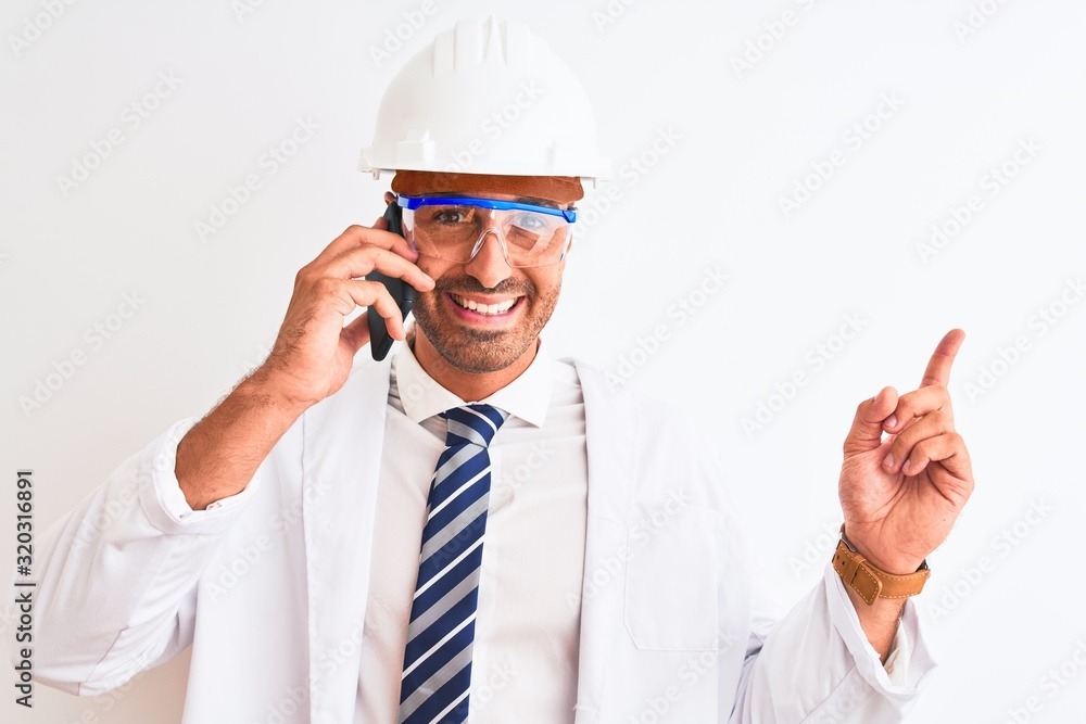 Young scientist man wearing safety helmet and calling using smartphone over isolated background very happy pointing with hand and finger to the side Young scientist man wearing safety helmet and calling using smartphone over isolated background very happy pointing with hand and finger to the side