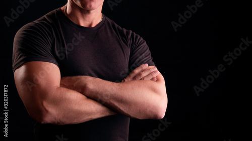 A man with strong arms. Male security guard in a black t-shirt. Strong man on a black background. Concept male security guard. photo