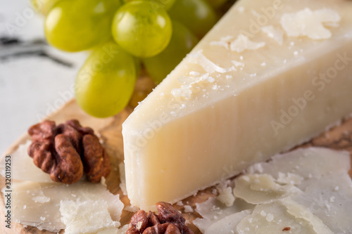 Pecorino romano, hard italian sheep milk cheese on wooden cutting board with grape, selective focus