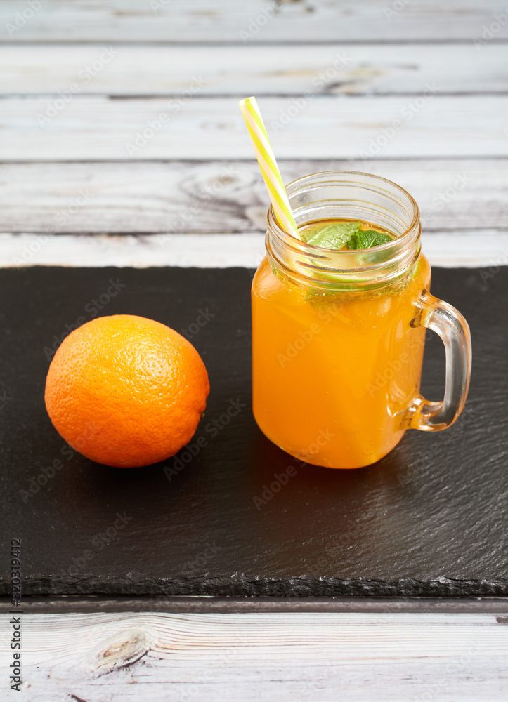 Fresh orange with oranges on a slate board on a light wooden background. Summer refreshing drink..Fresh orange in a glass jar with mint and oranges. Fresh orange with oranges on a slate board on a light wooden background. Summer refreshing drink..Fresh orange in a glass jar with mint and oranges.